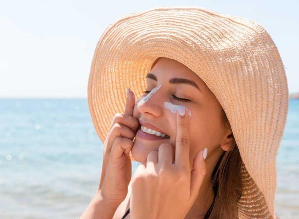 a young woman applies sunscreen to her face at a beach